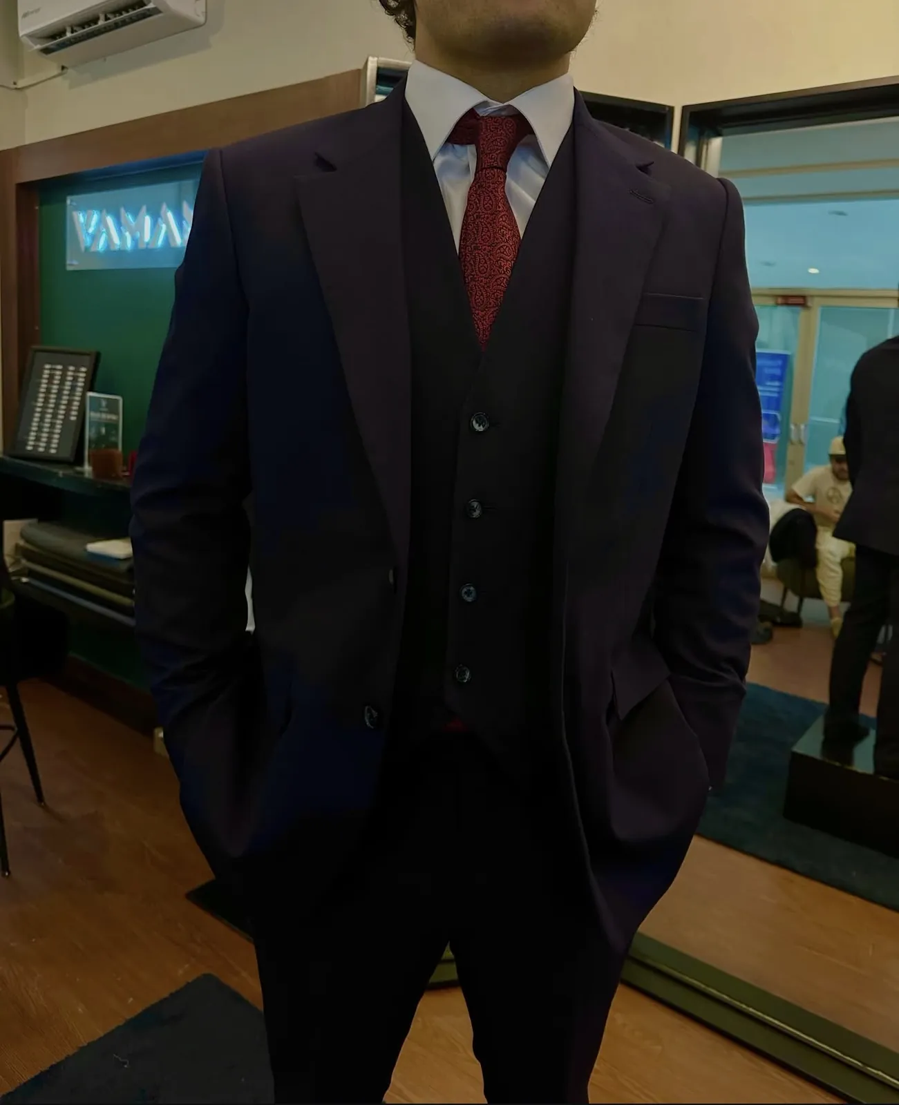 Novio con traje de tres piezas burdeos y corbata roja en el atelier VAMANA