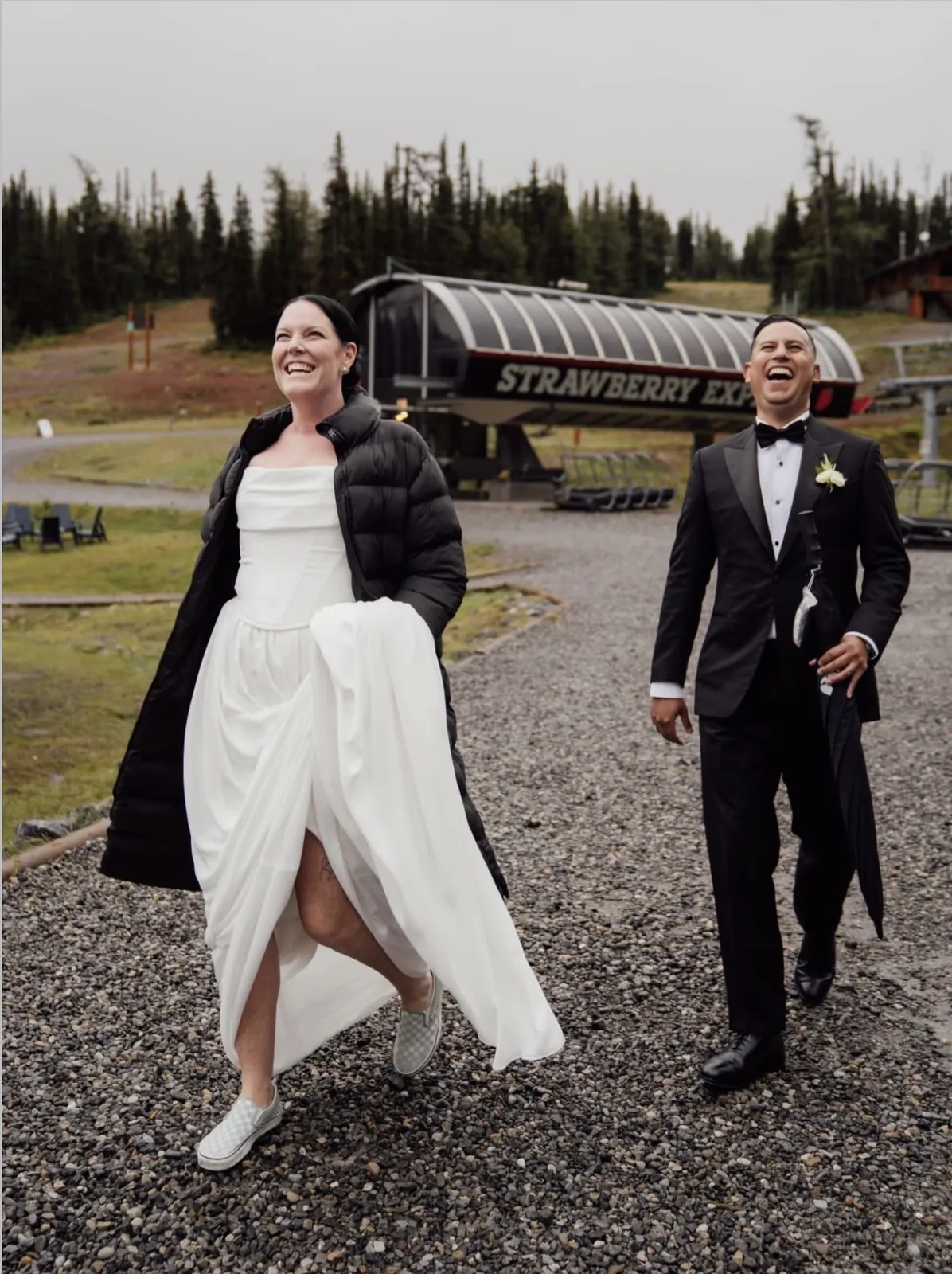 Novios caminando por la montaña, ella en vestido blanco y él en esmoquin negro