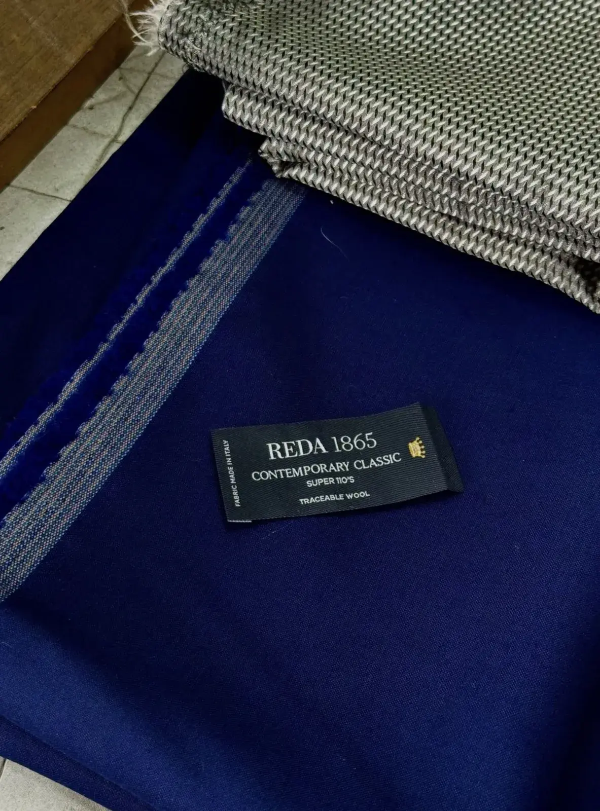 Detalle de tela azul con etiqueta REDA 1865 y tejido a cuadros en el taller